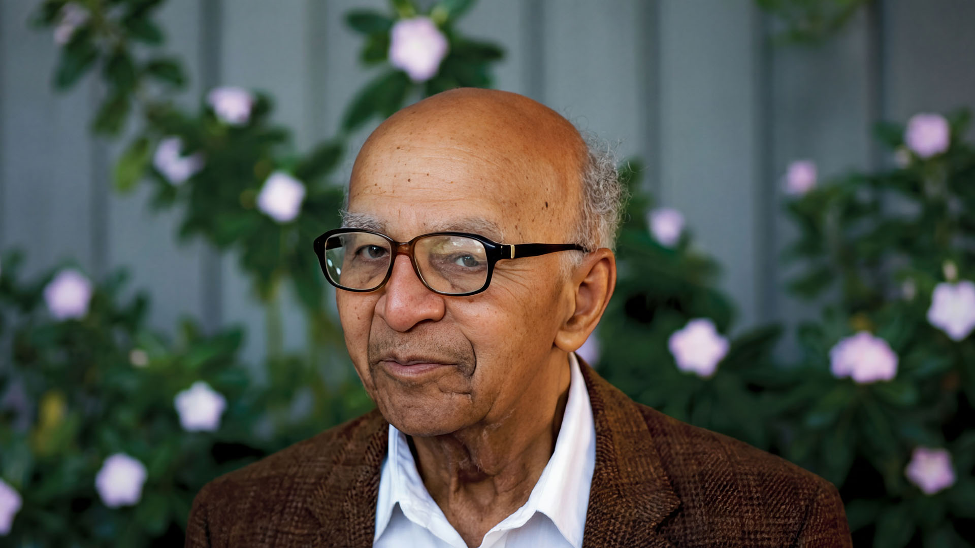 Portrait of David Blackwell wearing glasses with flowers in the background